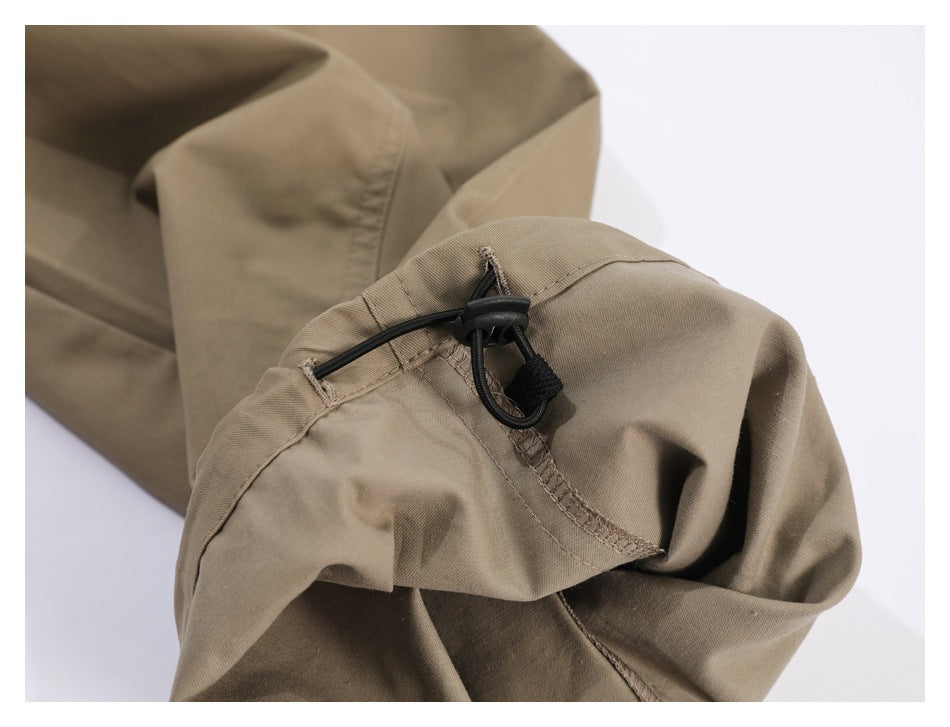 Close-up of a black elastic cord and toggle at the hem of taupe trousers.