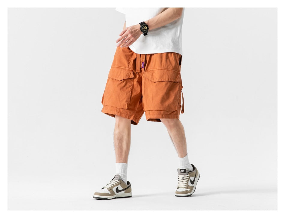 Front view of a model wearing rust-orange cargo shorts with large flap pockets and a white T-shirt.