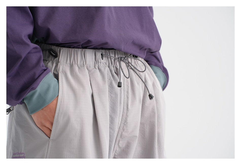Close-up of light gray pants showing the elastic drawstring waistband, front pockets, and stitching.