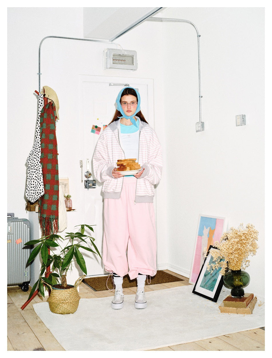 Front view of a model wearing a pale pink-and-white striped zip hoodie with gray trim and pink joggers.