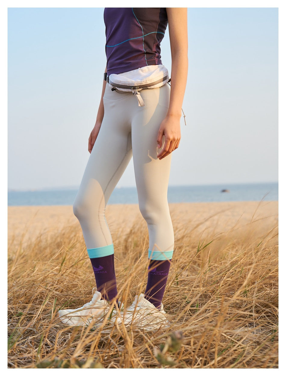 Cropped view of a person wearing pale leggings with turquoise ankle bands and purple socks, plus a waist pouch.