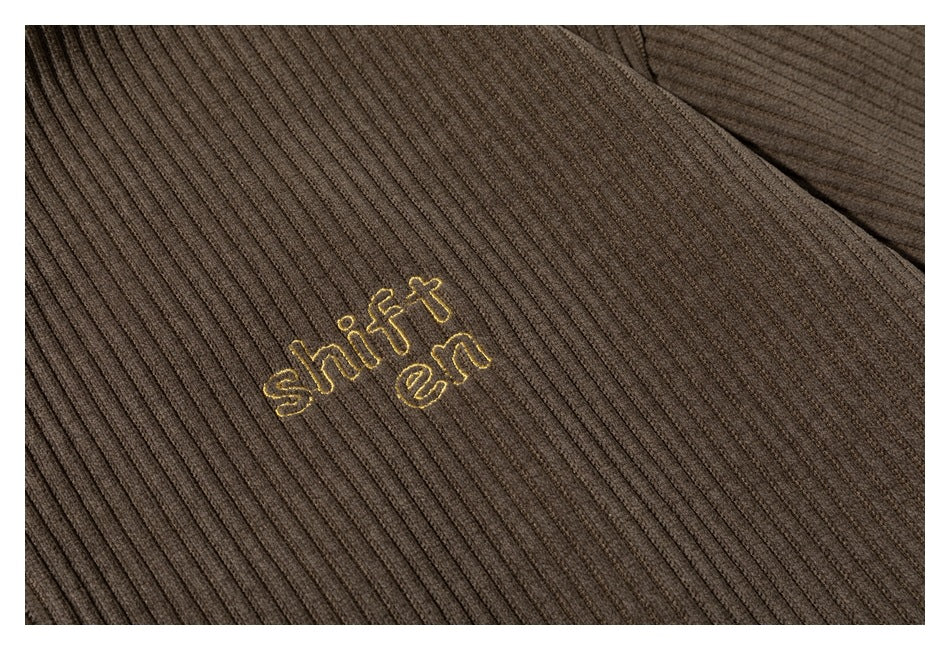 Close-up of brown ribbed fabric with small gold embroidered “shift en” lettering.