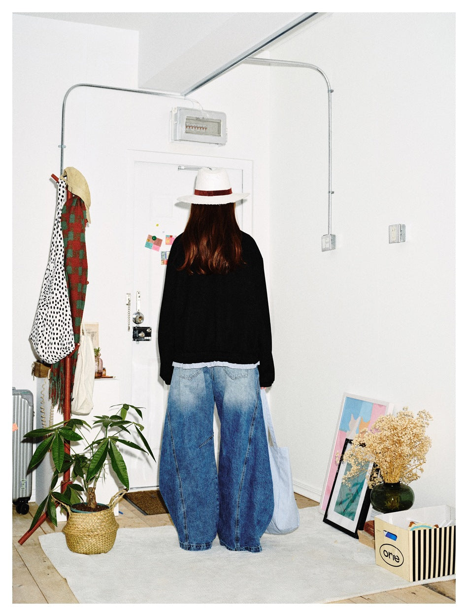 Back view of a model wearing a black jacket with a striped hem, paired with wide-leg blue jeans.
