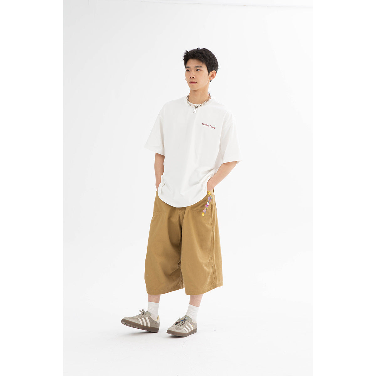 Model wearing a white oversized T-shirt with small red chest lettering and tan shorts.
