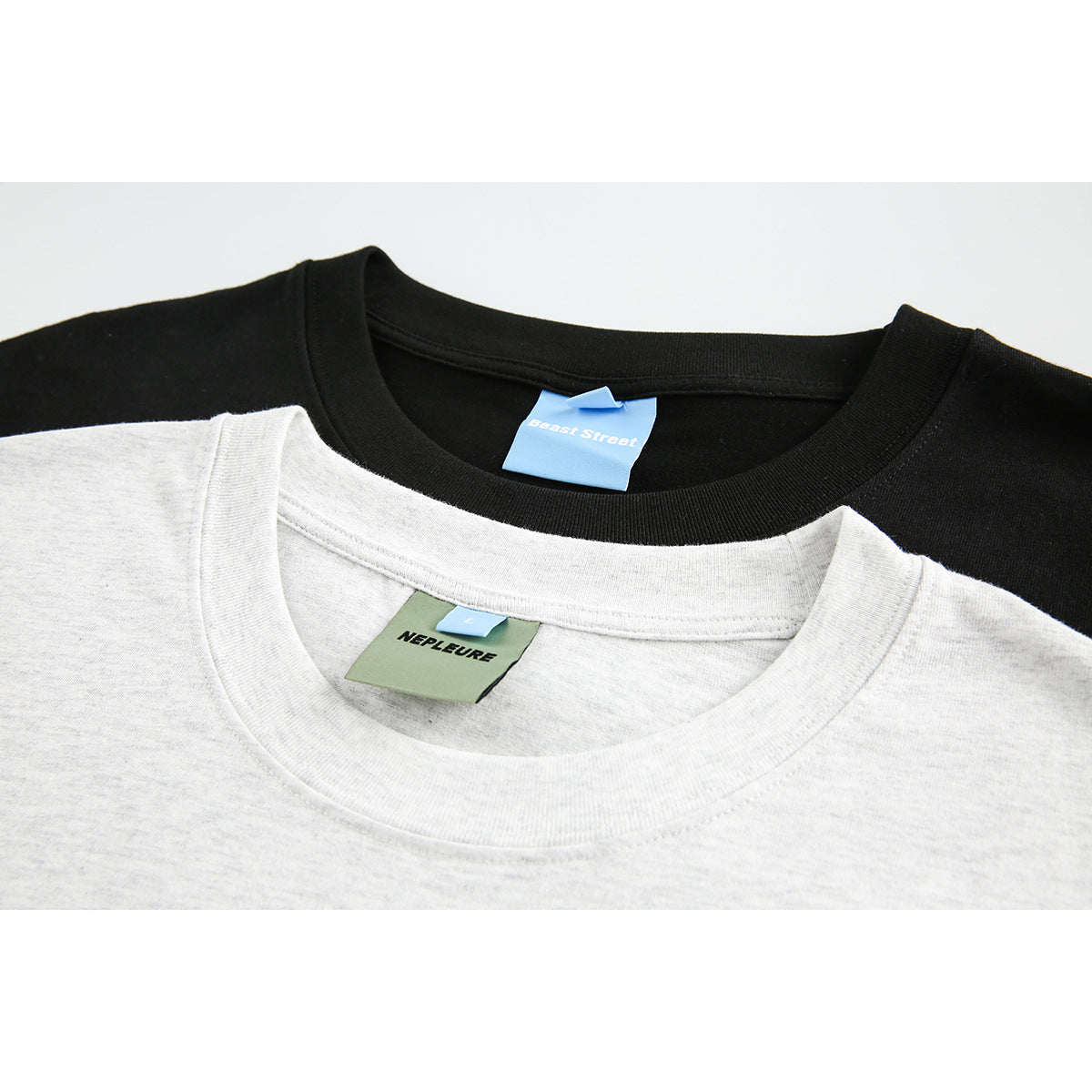Close-up of overlapping light gray and black T-shirt collars with visible neck labels.