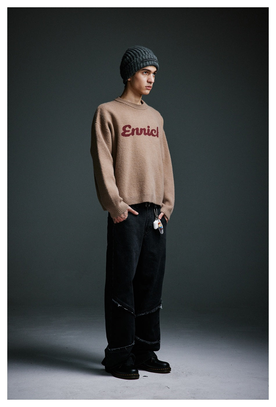 Model in camel Enrich knit sweater, gray beanie and black jeans, turned three-quarter side view