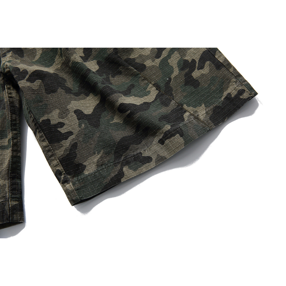 Close-up of the hem and stitched edge of olive and black camouflage trousers.