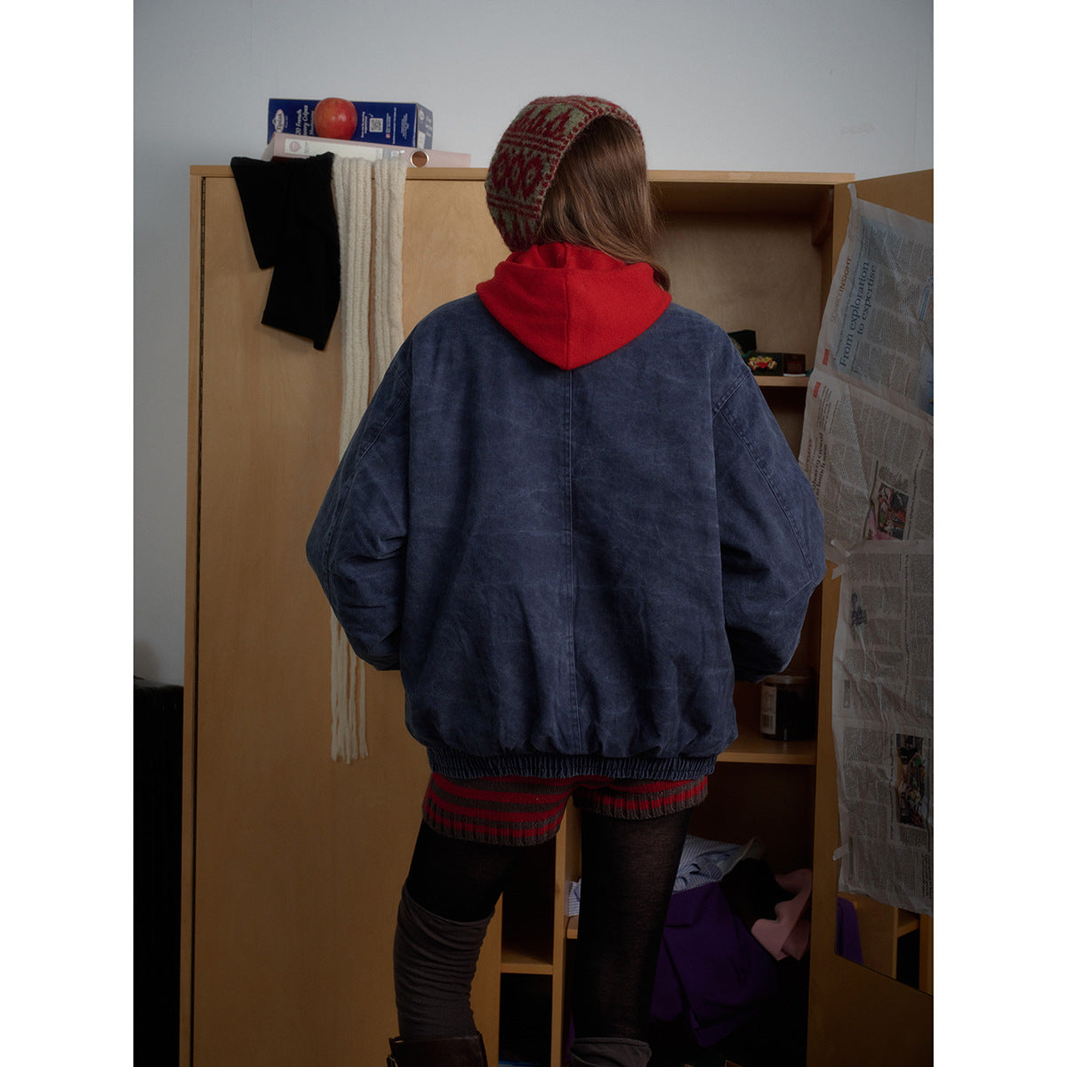 Back view of a model wearing an oversized navy washed jacket with an elastic hem over a red hood.