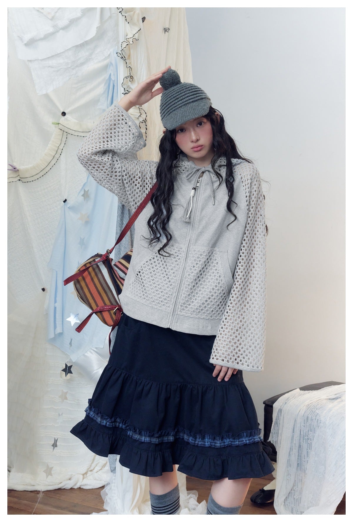 Front view of a model in a light gray open-knit sleeve hoodie and navy tiered ruffle skirt.
