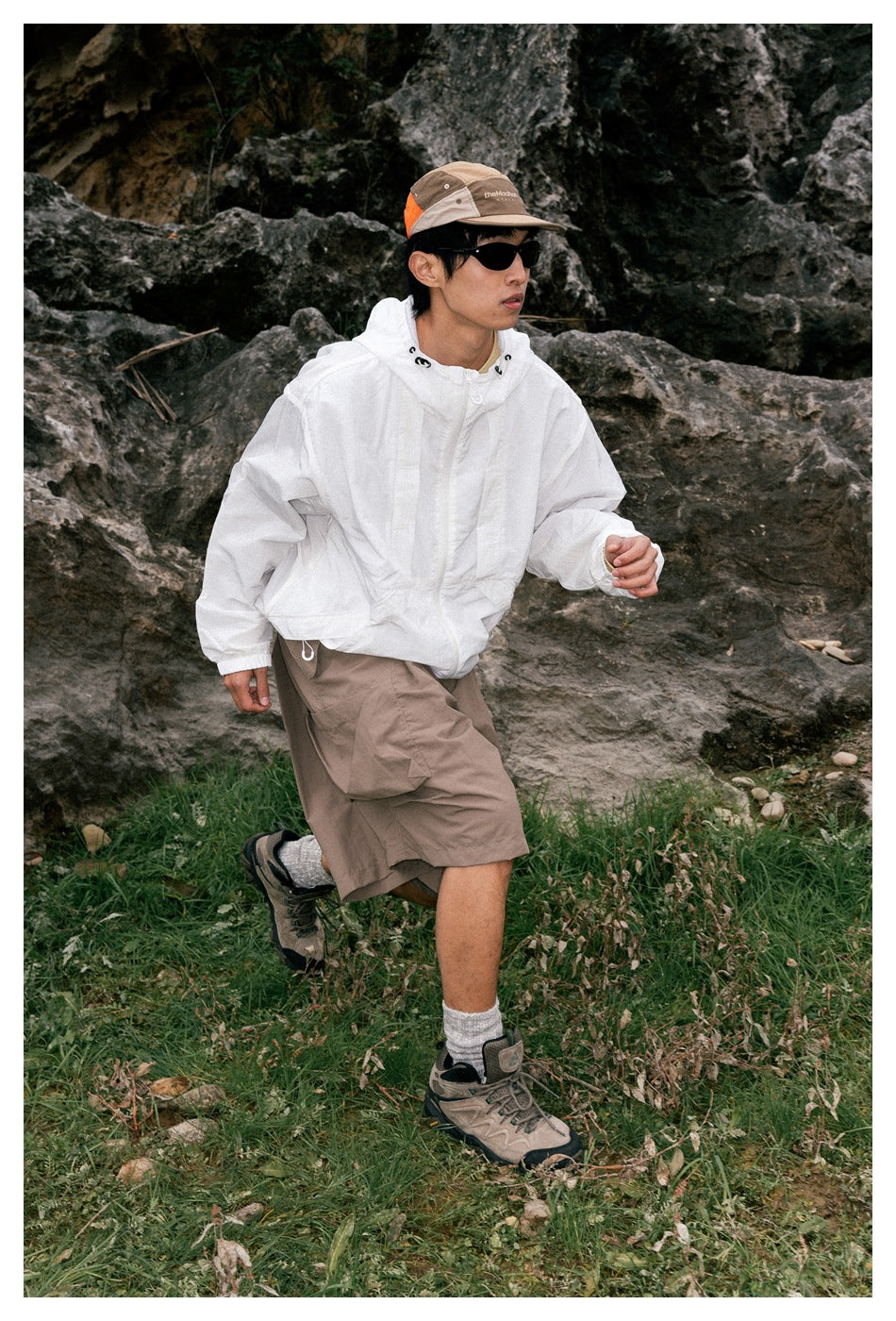 A man poses outdoors in a white hooded pullover and taupe cargo shorts with large side pockets.