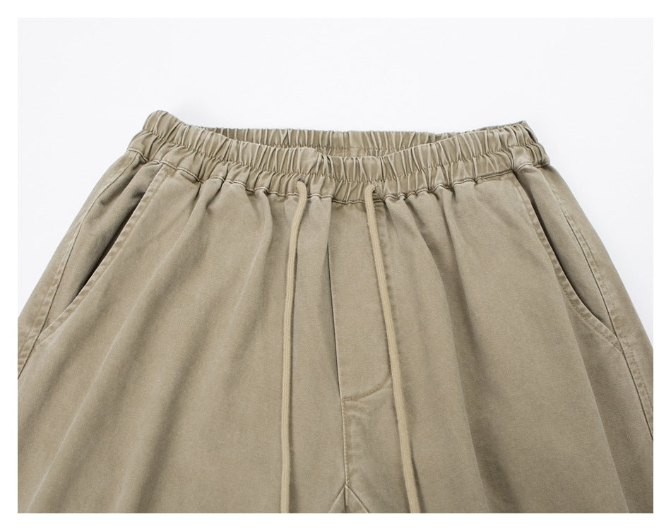 Close-up of beige pants showing the gathered elastic waistband, drawstrings, and angled front pockets.