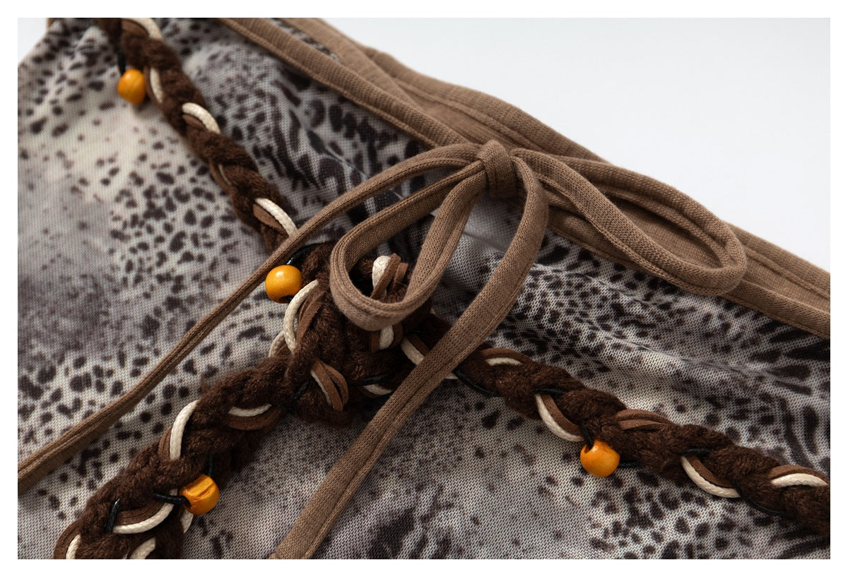 Close-up of a gray-brown animal-print garment with braided dark ties, tan cords, wooden beads, and a knotted drawstring.