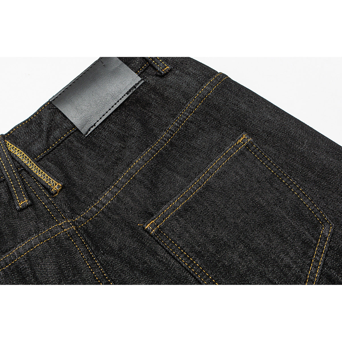 Close-up of dark indigo jeans showing a rear pocket, waistband and plain black patch.