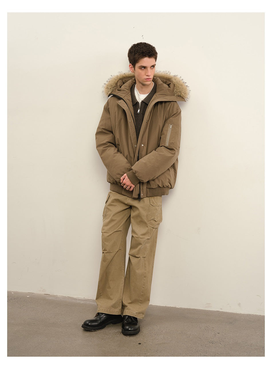 Model wears a taupe padded jacket with a beige fur-trimmed hood and tan cargo trousers, standing with hands clasped.