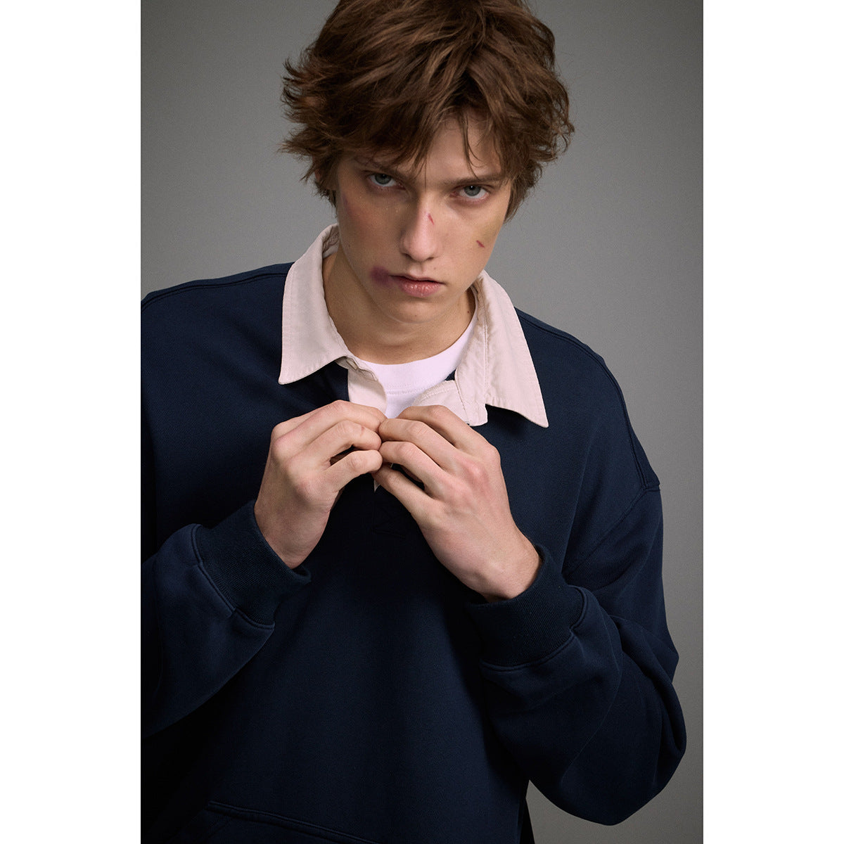 Close view of a model wearing a navy pullover over a pale pink collared shirt.
