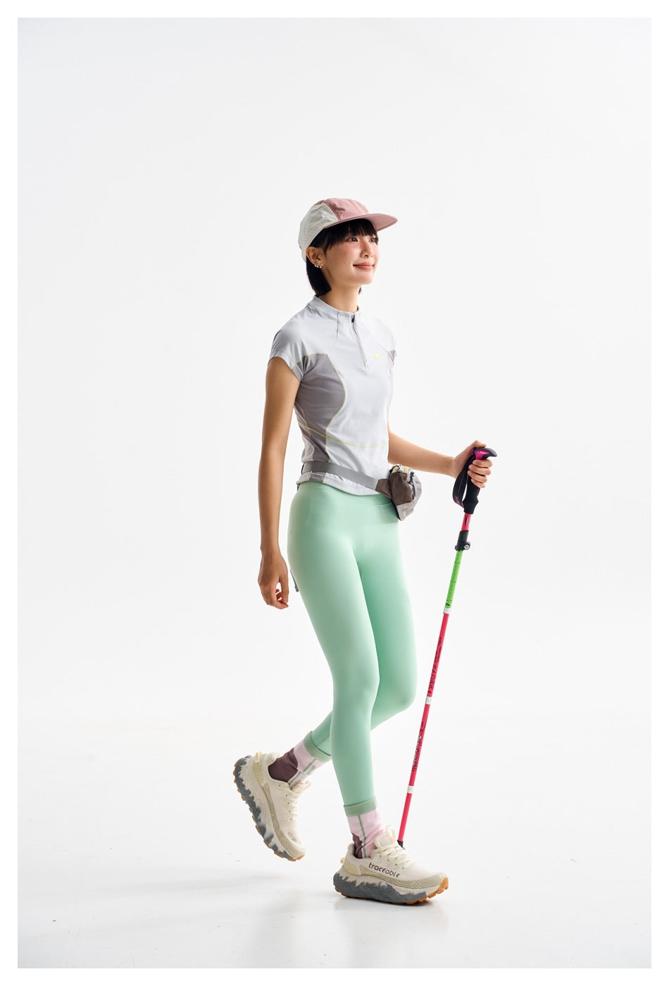 Model in a light gray short-sleeve quarter-zip top with gray panels, mint leggings, and a waist pouch.
