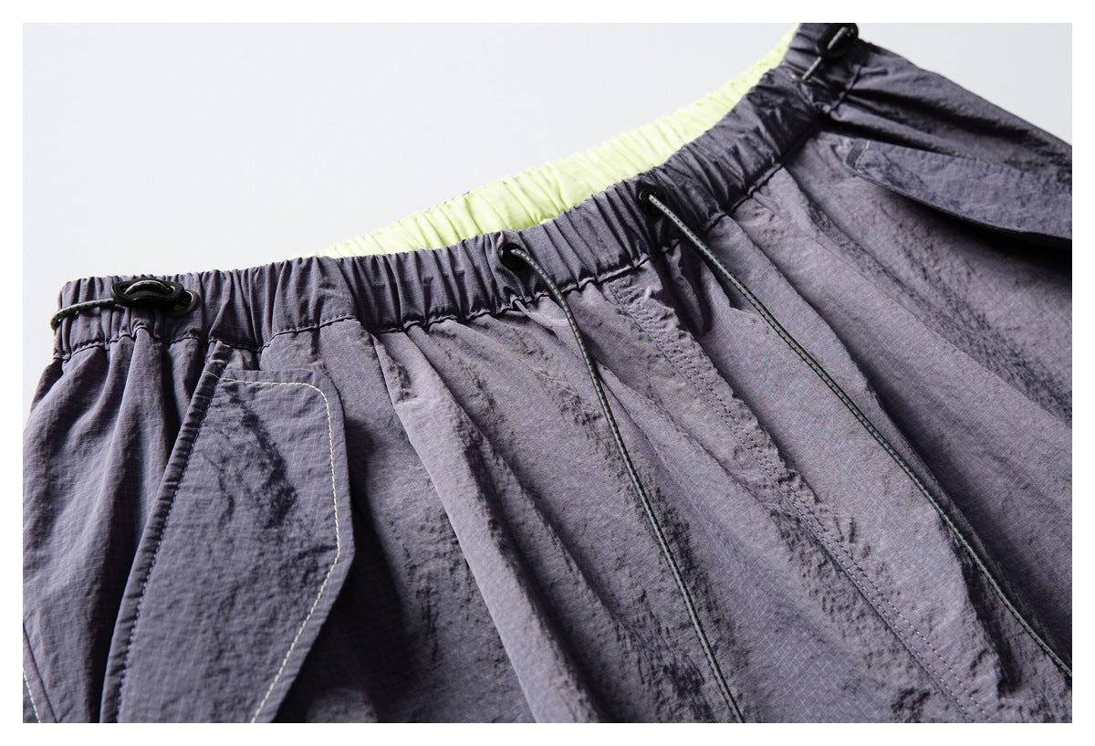 Close-up of charcoal-gray pants showing the elastic drawstring waistband, pocket construction, and pale lime lining.