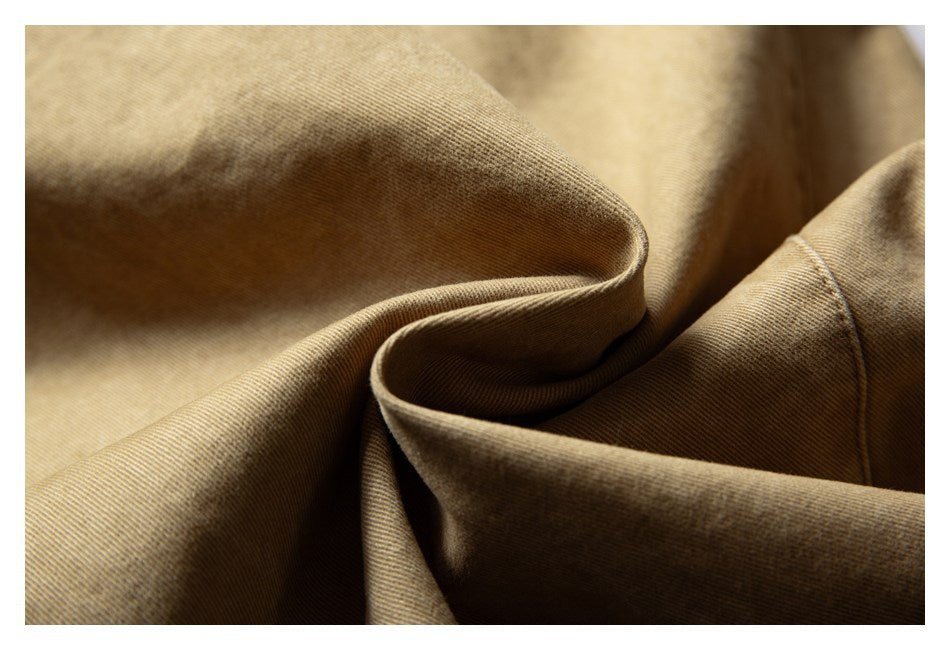 Close-up of tan trouser fabric draped into folds, with a stitched seam visible.