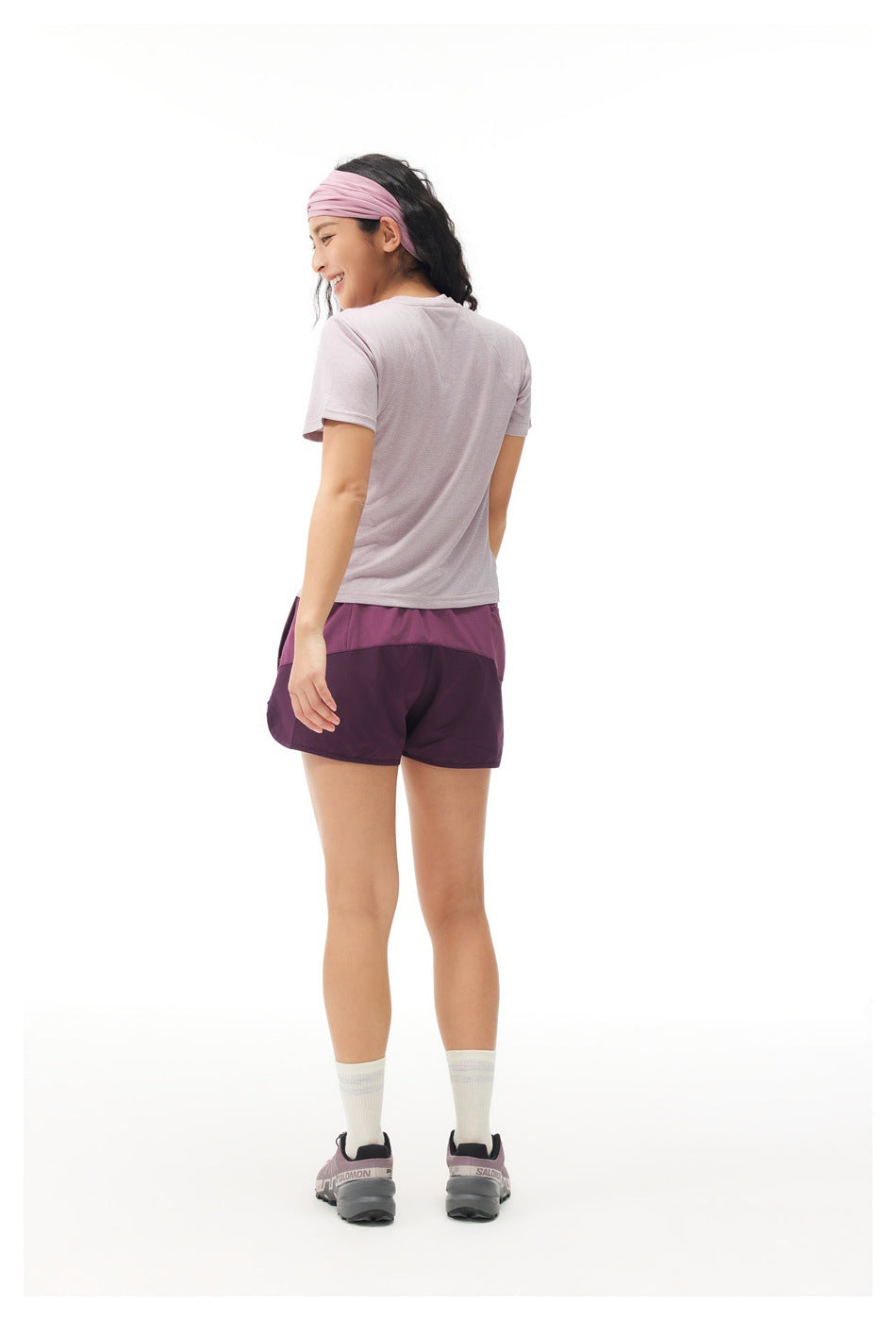 Rear view of a woman wearing a pale lilac short-sleeve shirt and plum running shorts.