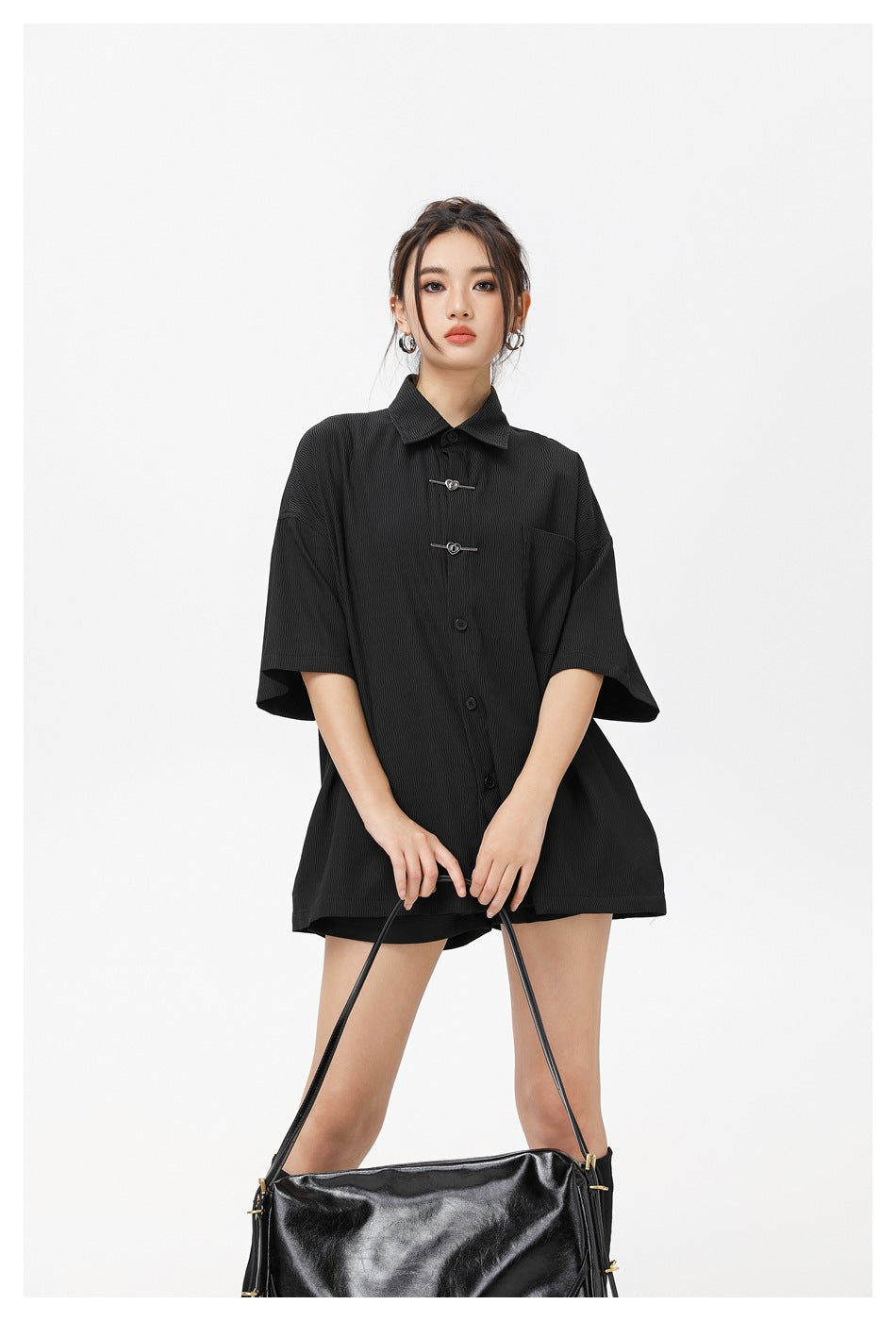 Model wearing an oversized black short-sleeve button-up shirt with a pointed collar, chest pocket and decorative front