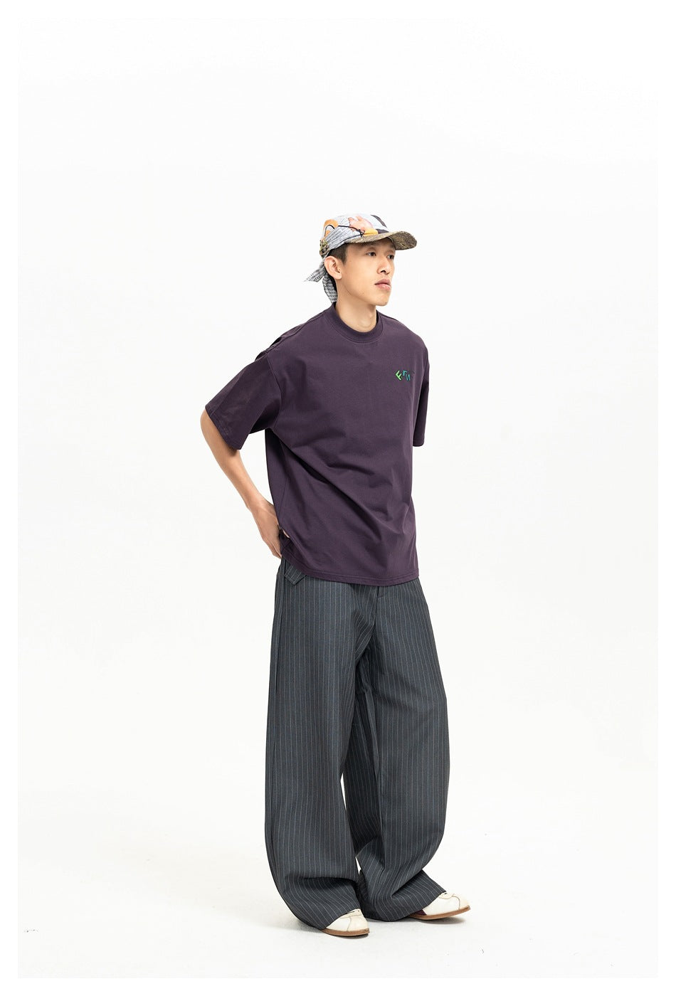 Three-quarter view of a model in a dark plum oversized T-shirt with a small green chest graphic and pinstriped wide-leg