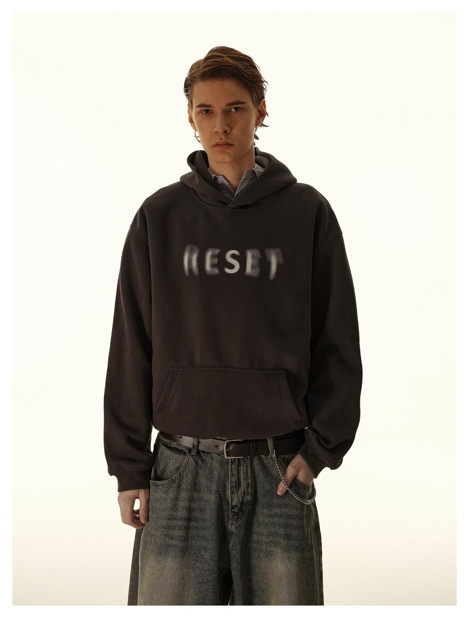 Model wearing a dark gray RESET print hoodie with wide-leg washed jeans, front view