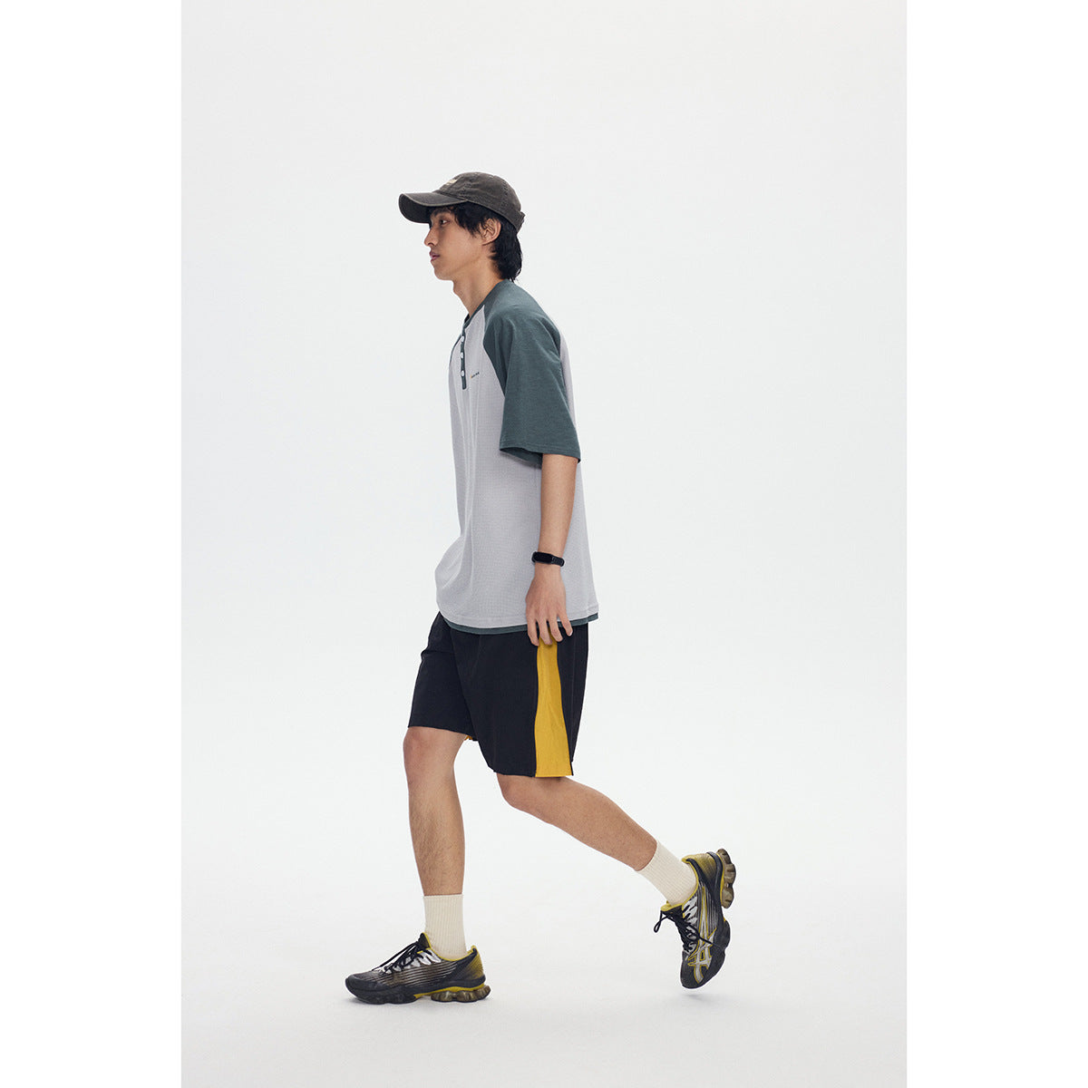 Model in a gray raglan T-shirt and black shorts with a yellow side panel, shown in profile.