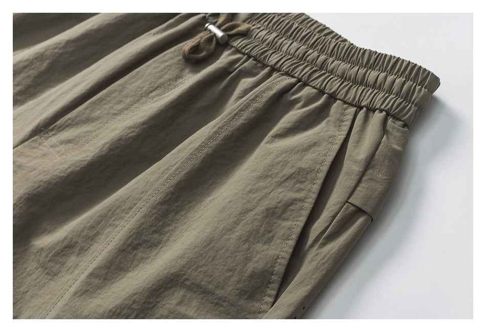 Close-up of olive-gray shorts showing the gathered waistband, stitching, and side pocket opening.