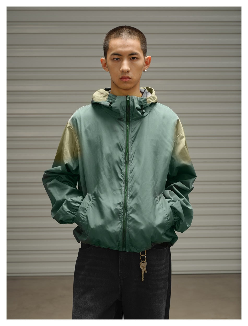 Closer front view of a sage green zip jacket with a hood, olive shoulder accents and two front pockets, worn by a model.