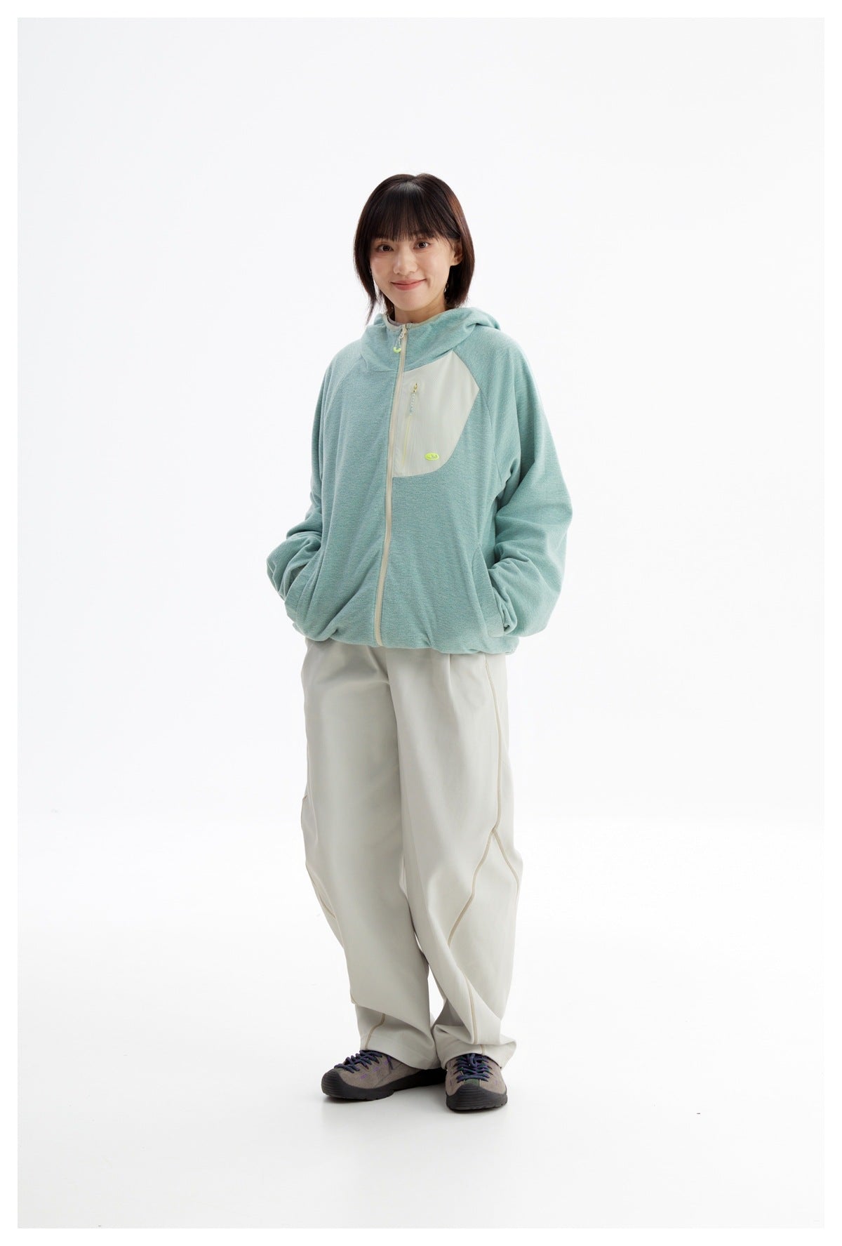 Three-quarter view of a model wearing a mint-green hooded zip jacket and loose ivory pants.