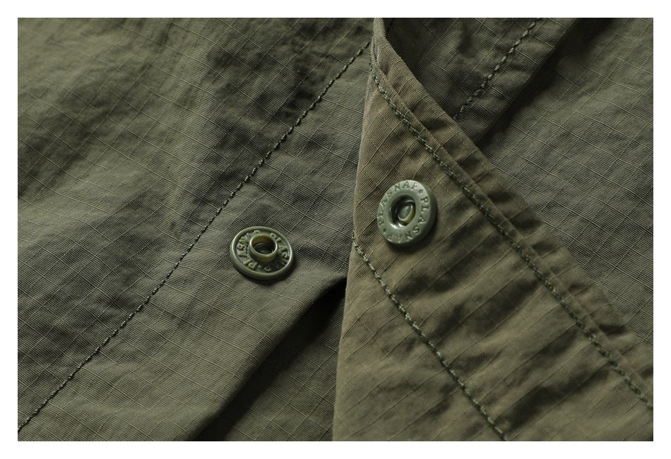 Close-up of olive-green fabric and two embossed snap fasteners along a stitched placket.