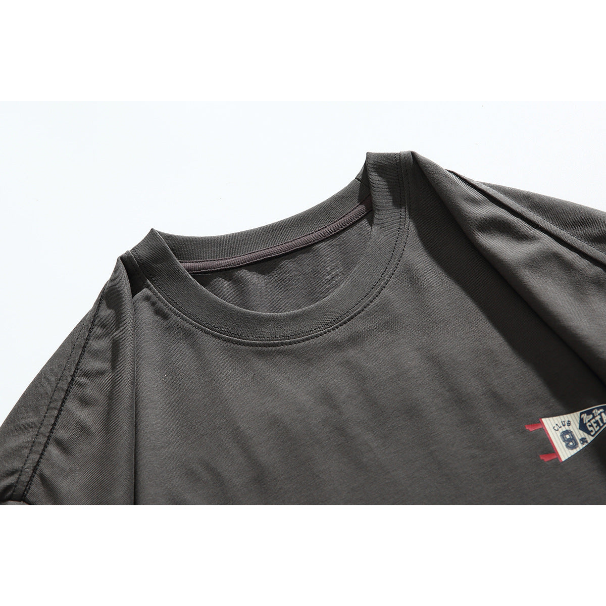 Close-up of a charcoal T-shirt's crew neck and shoulder seam, with part of a small chest graphic visible.