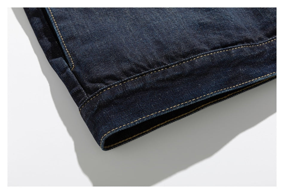 Close-up of the folded hem of a dark indigo denim jacket with golden double-row stitching.