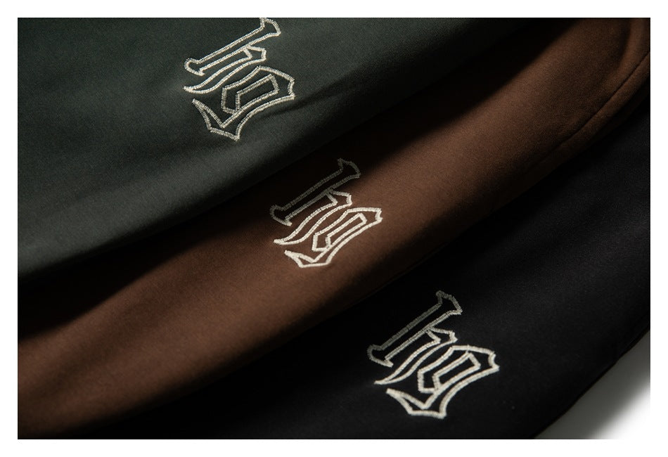 Close-up of dark green, brown, and black pants with the same embroidered light-colored emblem.