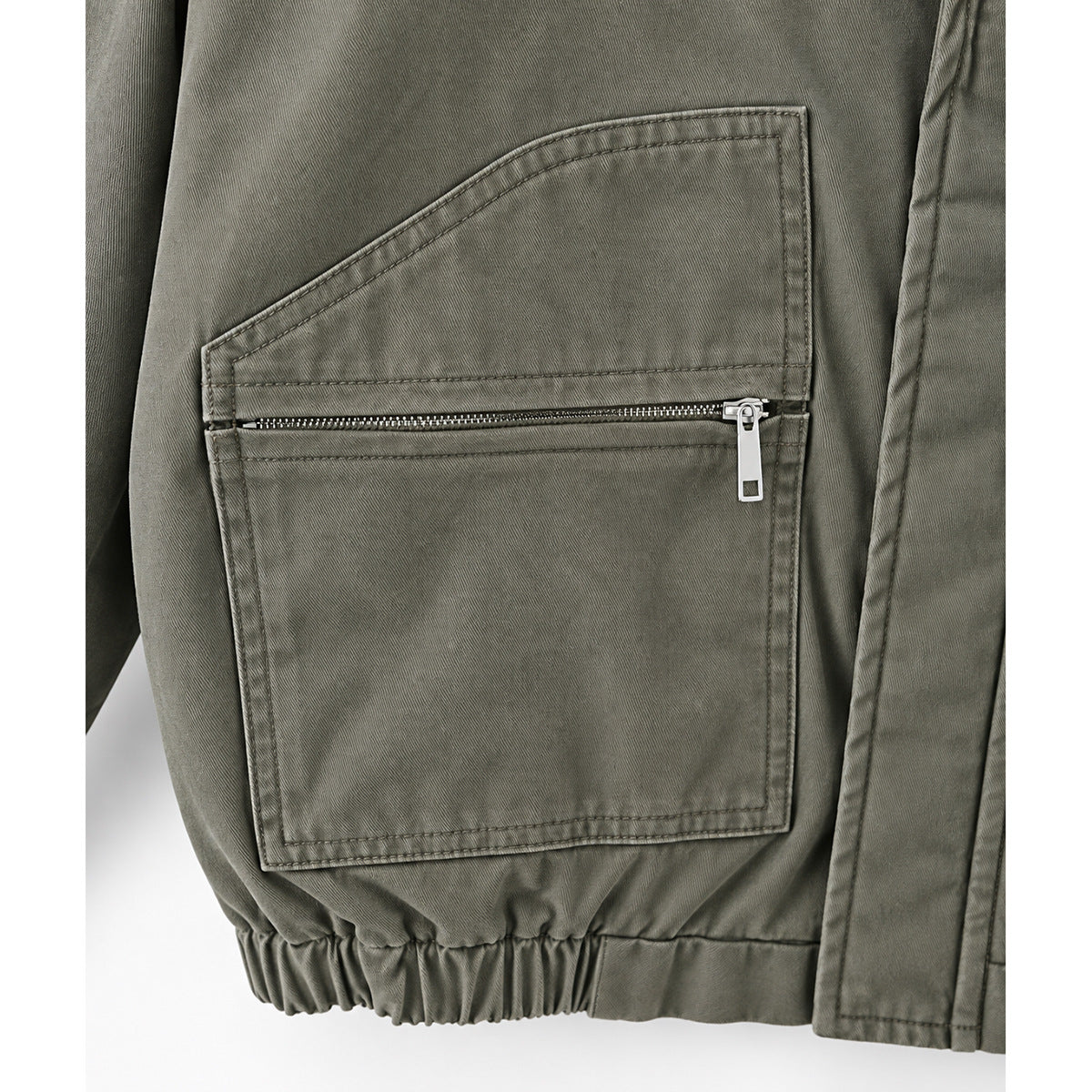 Close-up of an olive-gray jacket's large rectangular pocket with a horizontal zipper and elastic hem.