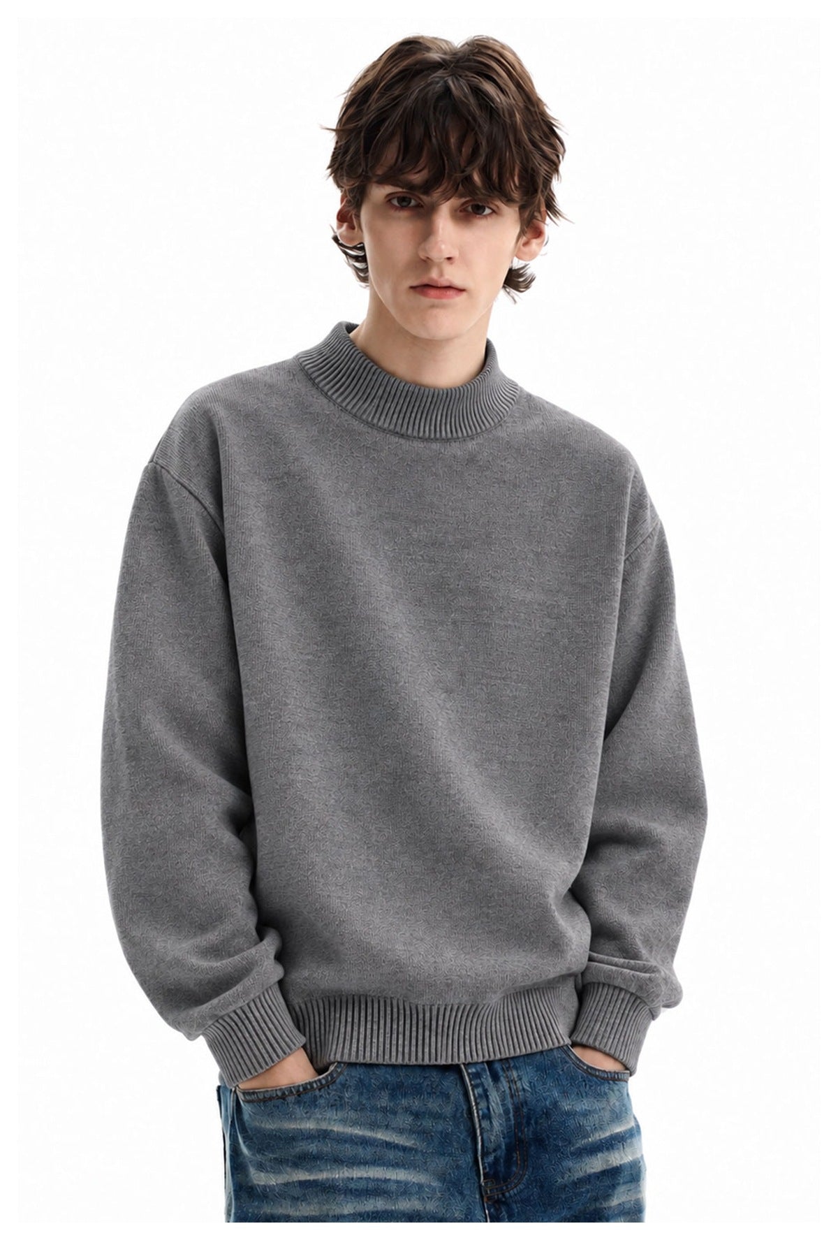 Man wearing a textured gray high-neck sweater with ribbed collar, cuffs and hem, paired with blue jeans.