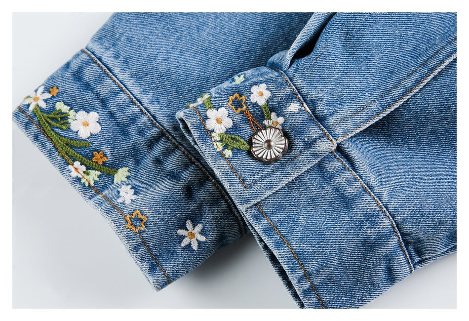 Blue denim cuff with white and yellow floral embroidery and a decorative silver button.