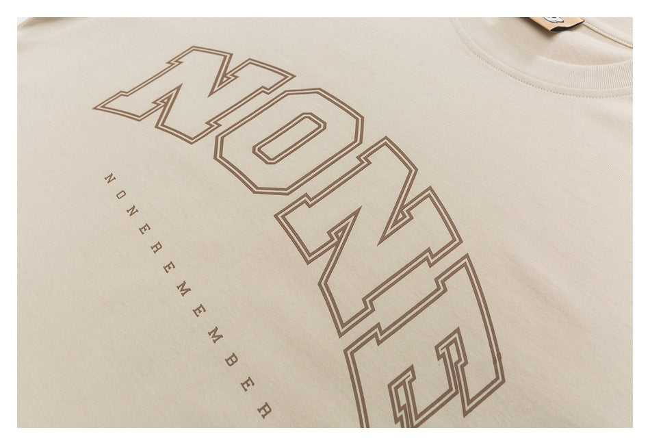 Close-up of a beige T-shirt with large brown outlined lettering and smaller spaced text printed on the chest.