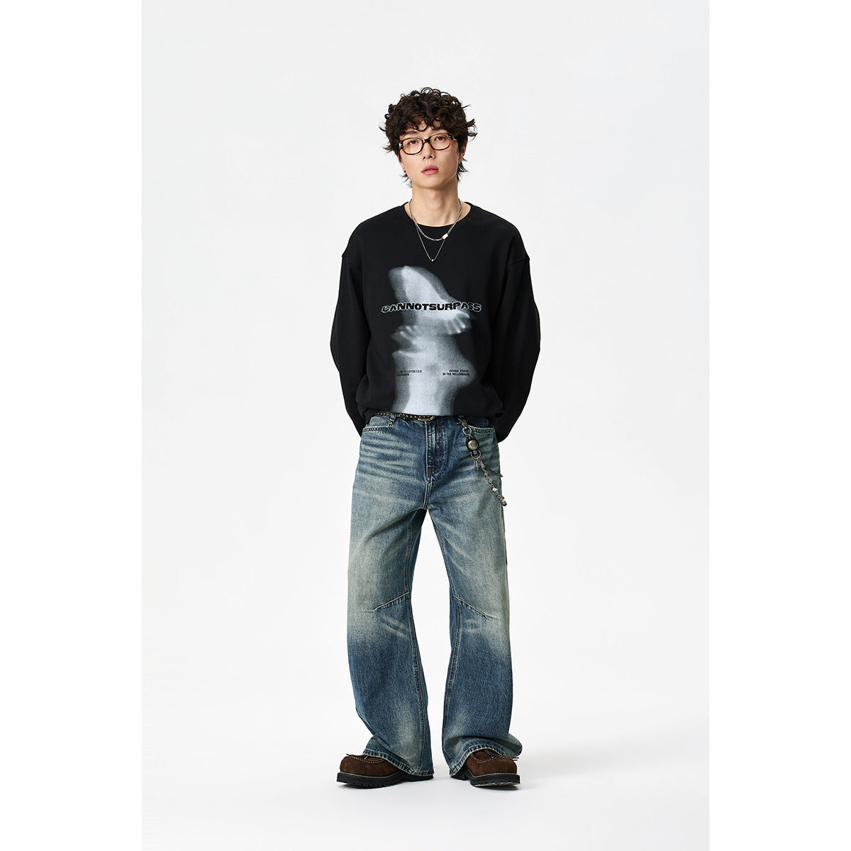 Model wearing a black long-sleeve shirt with a large gray front graphic and loose blue jeans; front view.