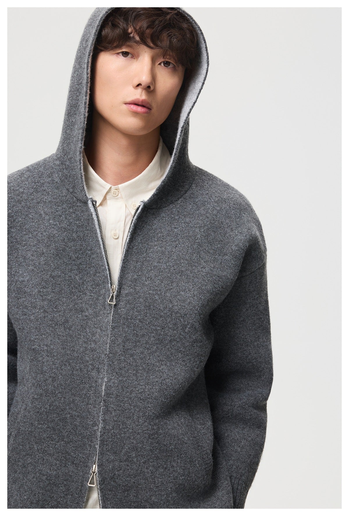 Close view of a model wearing a charcoal hooded cardigan, showing its zipper, hood, and textured knit.