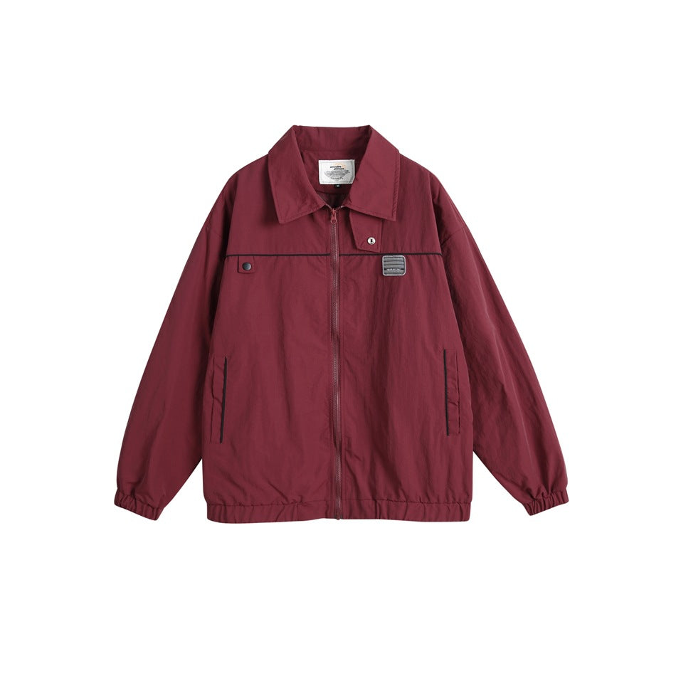 Wine red zip-front jacket with turn-down collar, black piping, chest patch, side pockets and elastic cuffs, flat lay