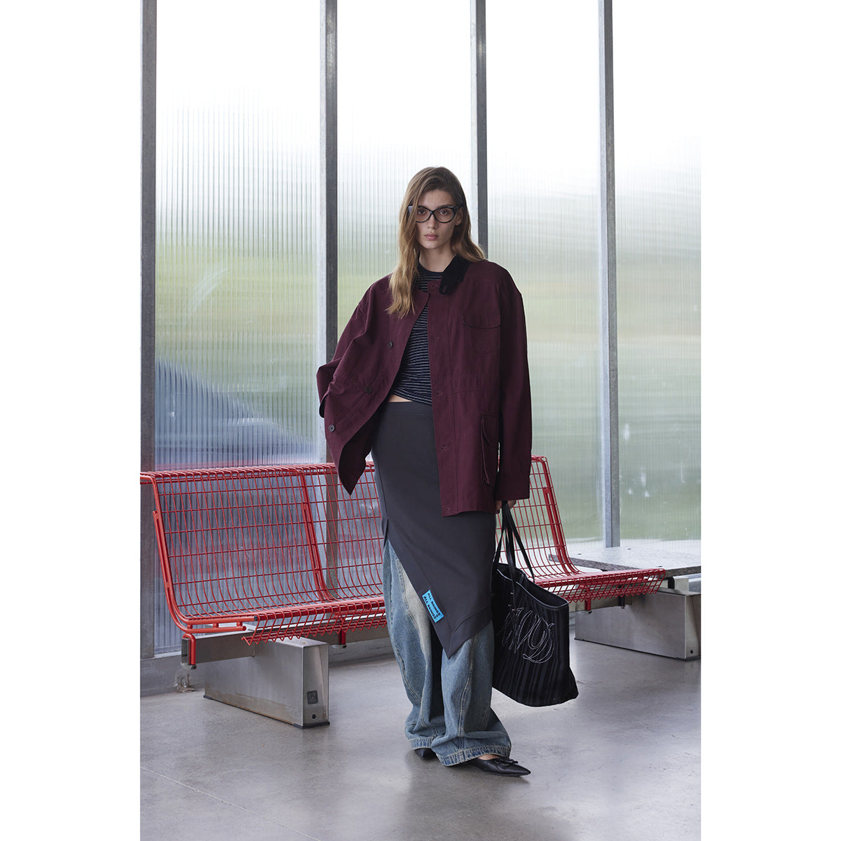 Full-length view of a model in a burgundy utility jacket with a black collar and flap pockets.