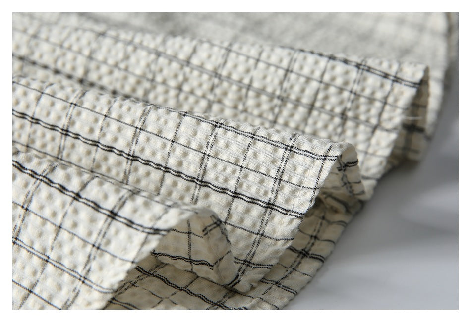 Close-up of a folded edge and stitching on the off-white shirt's black windowpane-check fabric.