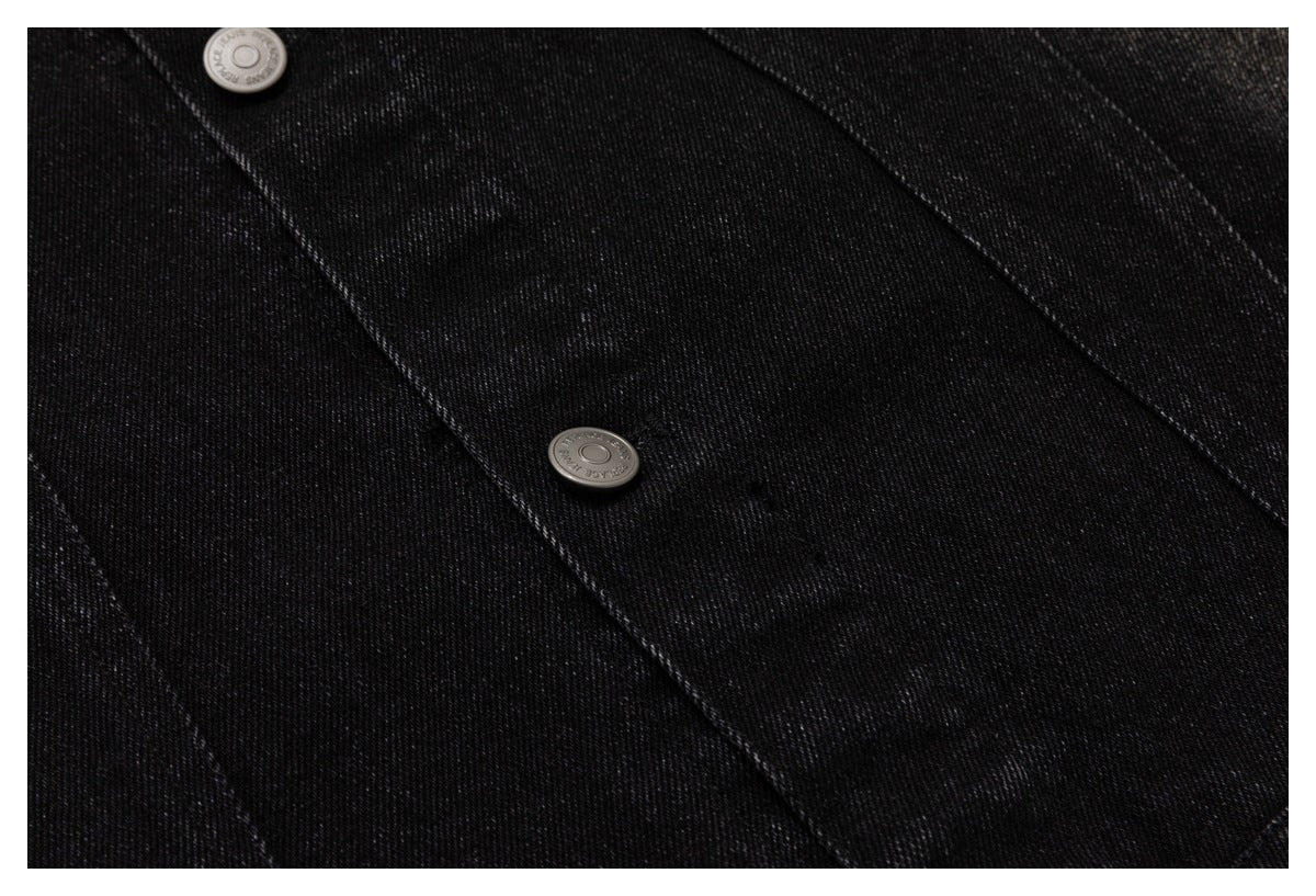 Close-up of black denim jacket panels, topstitching, and two metal buttons.