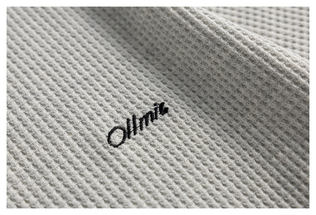 Close-up of a light gray ribbed knit garment with small black embroidered lettering.