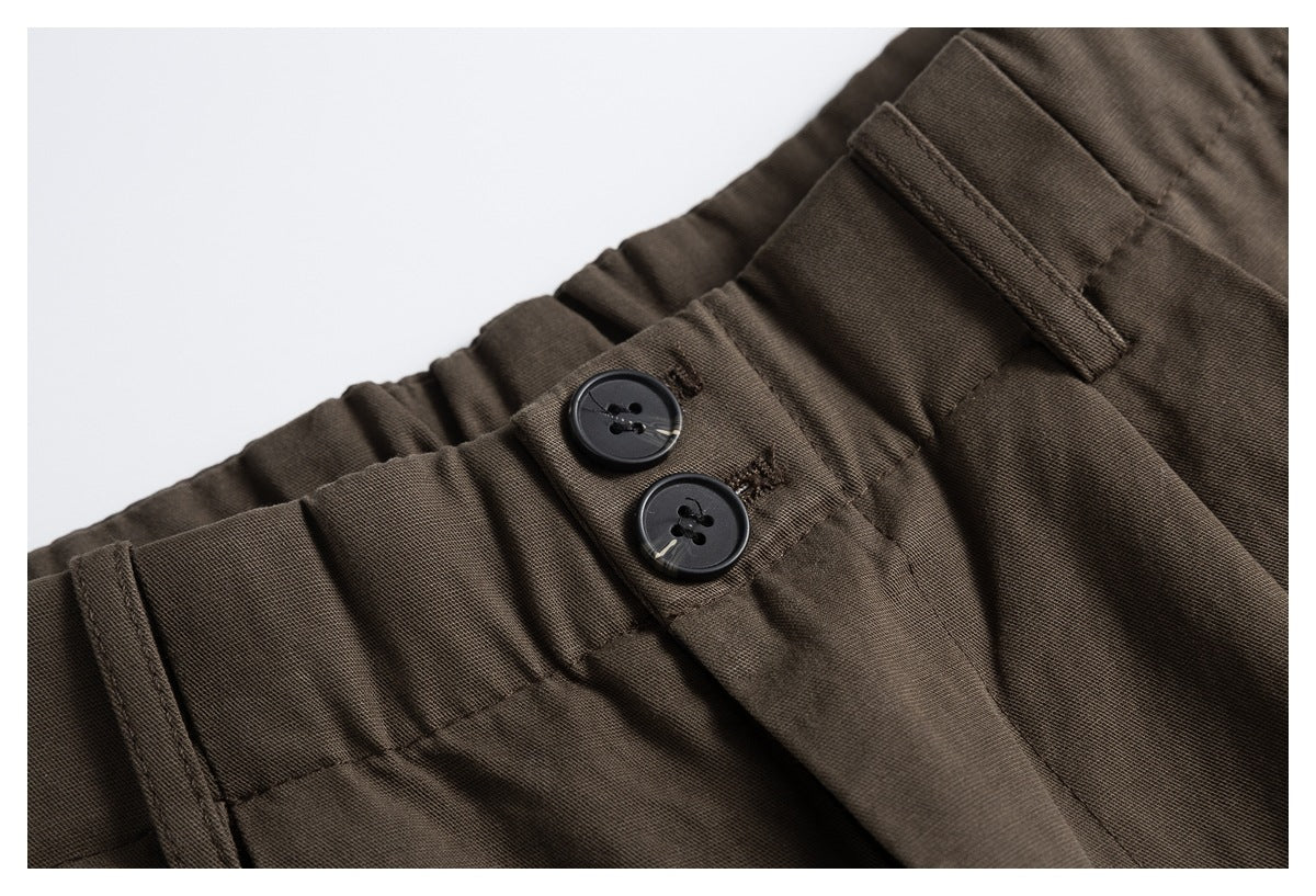Close-up of brown trousers showing two black buttons, a belt loop, and the gathered waistband.