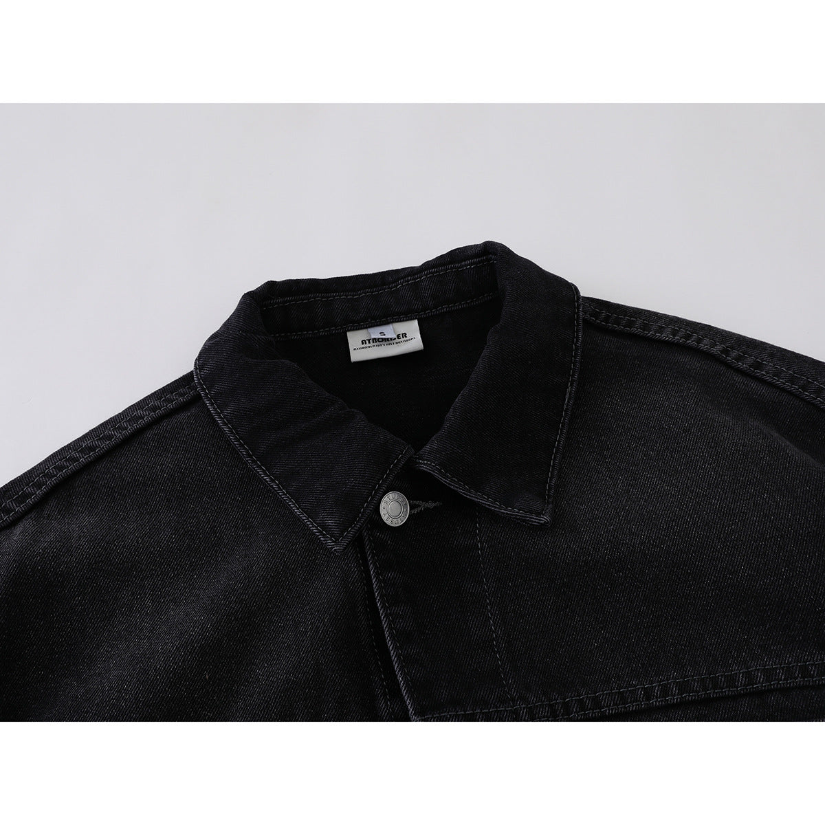Close-up of a black denim jacket collar, top button, shoulder seams, and inner neck label.