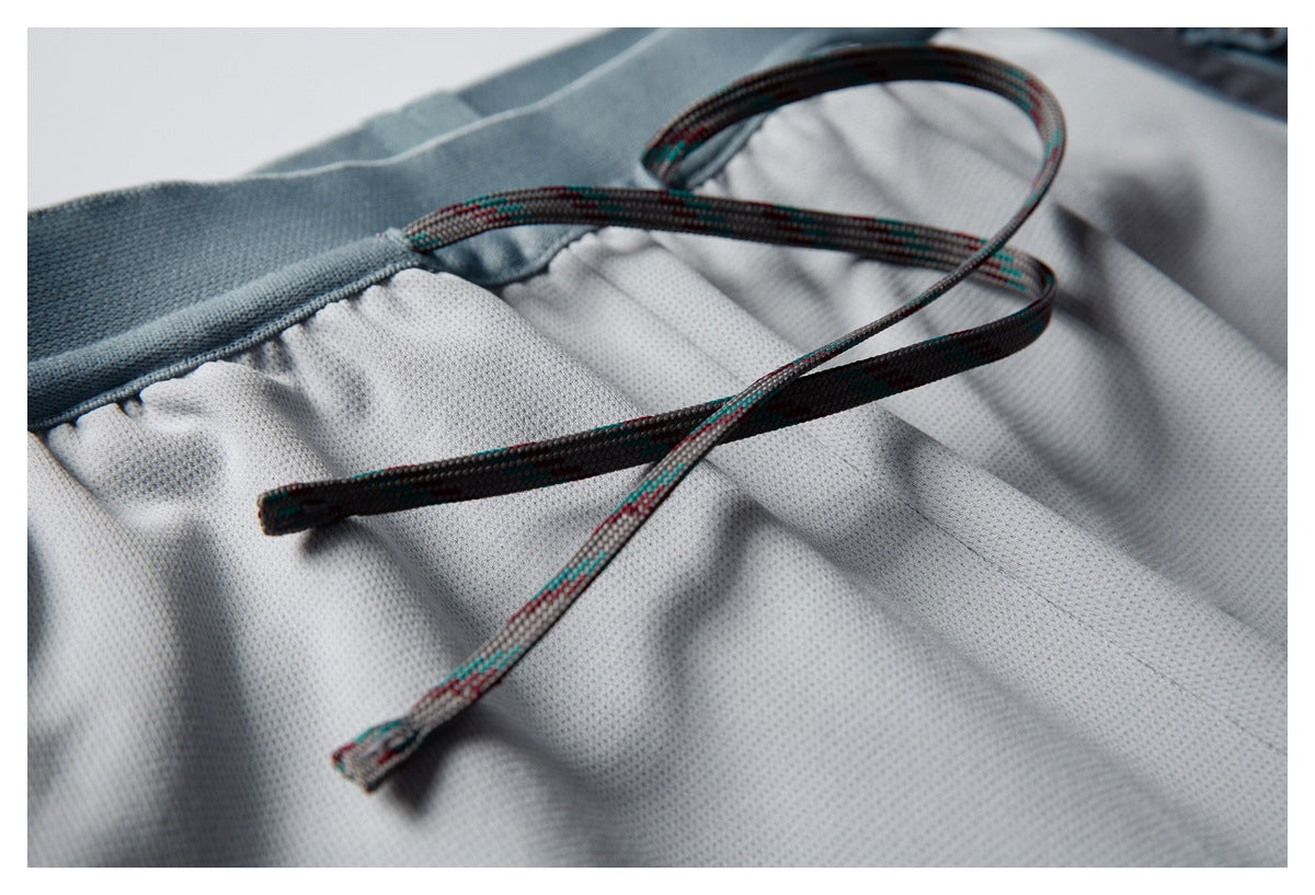 Close-up of the patterned drawstrings and gathered waistband on the light gray pants.