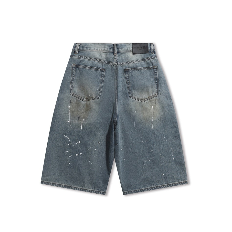 Back of faded blue denim shorts with two patch pockets, paint splatters, and a dark patch on the waistband