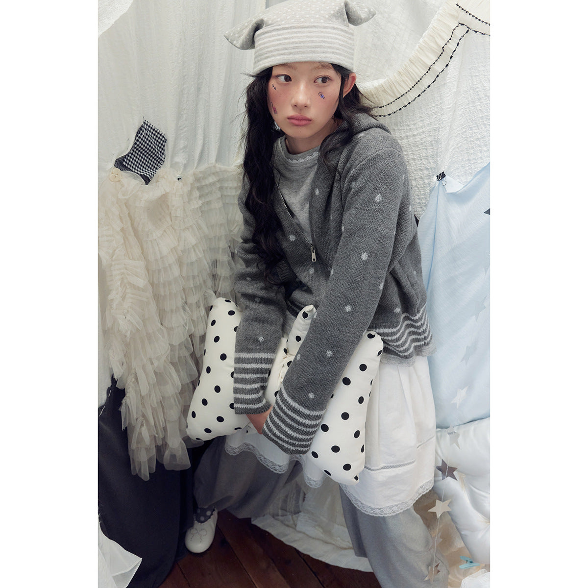 Close view of a model in a gray spotted zip hoodie with striped cuffs and a white skirt.
